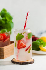 A refreshing summer drink with strawberries, lemon and mint in a glass on a light background. Strawberry lemonade