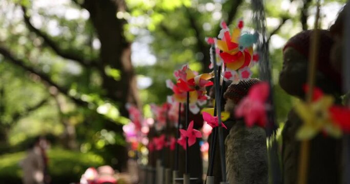 A slow motion of moving colorful windmills with Jizo statue daytime