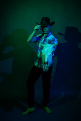 A guy in a cowboy hat and a plaid shirt in a studio with blue and green light