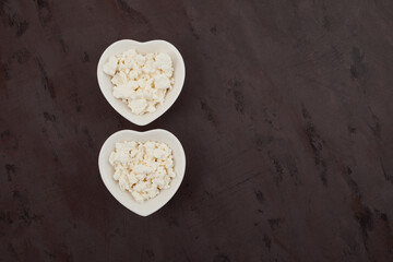 Chaana - homemade unripened cheese. Bengali cuisine. Cottage cheese in white bowls heart shaped on brown textured background. Top view, space for text