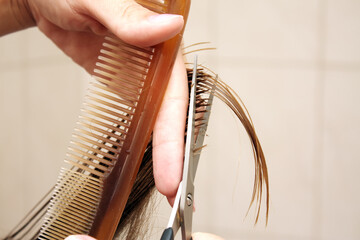 Hand of hairdresser cuts hair of woman close up in beauty salon.