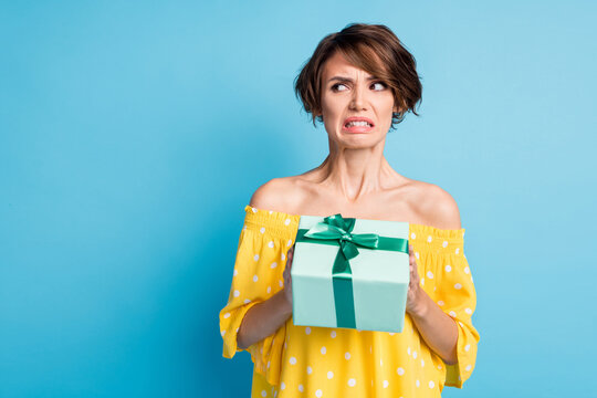 Photo Of Disgusted Young Woman Hold Dislike Gift Look Empty Space Bad Mood Isolated On Blue Color Background