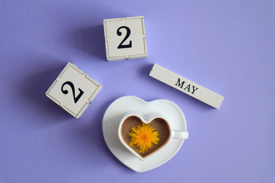 Calendar for May 22: cubes with the number 22, the name of the month of May in English, a cup of coffee in the shape of a heart with a dandelion flower, top view