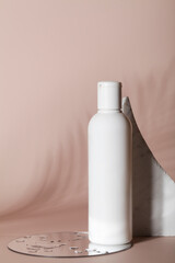 Mock up of white bottle lotion bottle with stone, mirror with water and tropical leaf shadow on beige background.Natural organic cosmetics concept.
