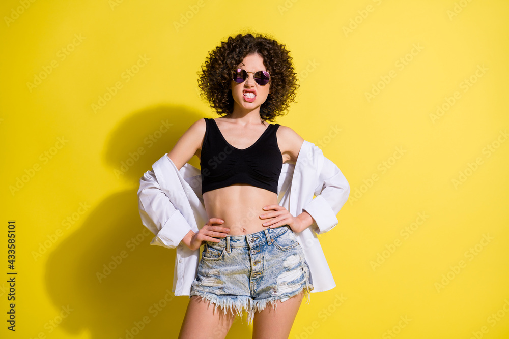 Sticker Photo of rude angry woman dressed black top dark eyewear arms waist showing teeth isolated yellow color background