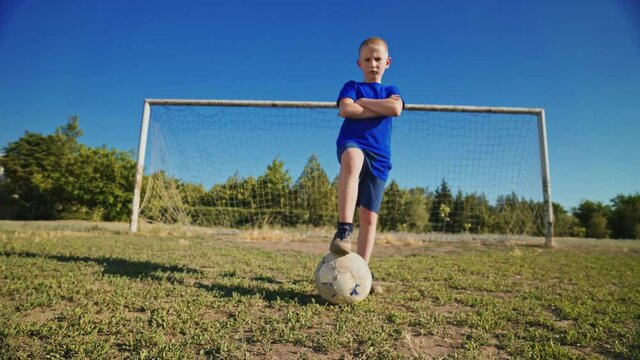 Defender at the football goal. The confident goalkeeper stares at the camera. Football concept. Young footballer with the ball under his foot.