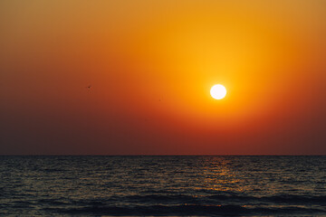 Scenic view of Sun setting in vibrant orange sky reflecting on the water