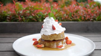 Close up of a stack of vegan pancakes decorated with plant based whipped cream and strawberries. Healthy breakfast concept