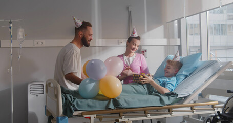 Mother and father visiting sick son in hospital ward and celebrating birthday together