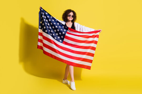 Full length body size photo of curly woman showing usa flag smiling wearing jeans shorts white shirt isolated bright color background