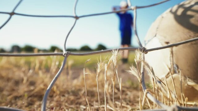 The young player rolls the ball into the net. Training day. Shots on goal. Street sports in a poor area of a city or village. The boy kicks the ball. Football concept.