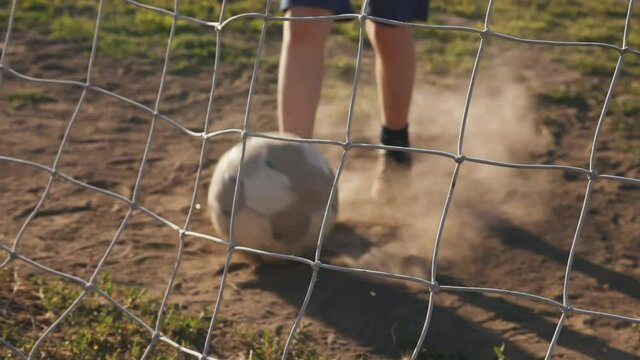 Shots on goal. The young player rolls the ball into the net. Training day. Street sports in a poor area of a city or village. The boy kicks the ball. Football concept. 