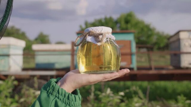Natural sweetness. Fresh honey in the  beekeeper's hands. Girl wearing a beekeeper's mask holding a jar of honey in her hands. A family honey business. Liquid sweet gold. 