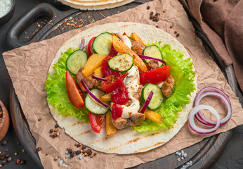 Pita bread with vegetables, meat and herbs on a brown background.