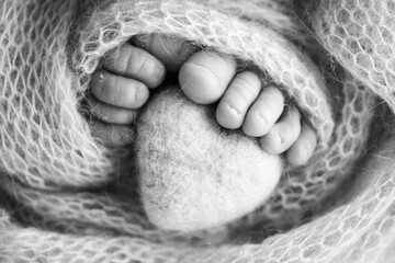 Feet of a newborn with a wooden heart, wrapped in a soft blanket. Black and white studio photography.