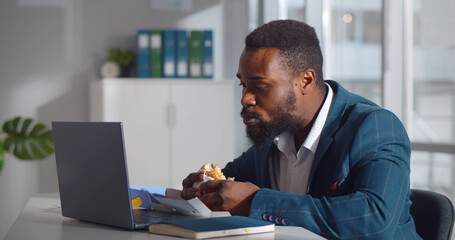 African male worker in office having fast food lunch at desk