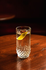 Gin and tonic cocktail in a highball glass served over ice, lemon twist garnish, at the wooden...