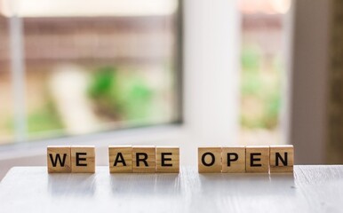 The word "we are open" made of wooden cubes on the background of an open door, End of quarantine, a cafe, a local shop, in welcoming guests after the coronavirus outbreak and the shutdown of people