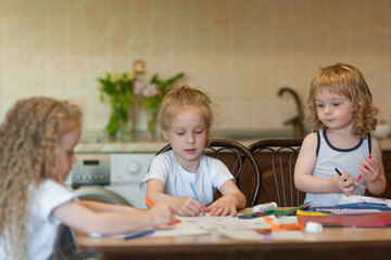 three children are engaged in creative work at the table at home: draw, cut the applique