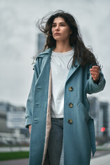 brunnette young girl in overcoat with skycraper behind her in the center of the modern city. Woman is standing in front of modern office buildings