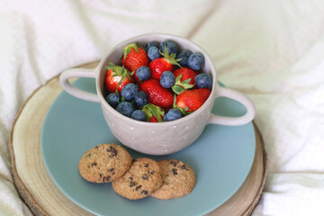 Bowl of blueberries and strawberries and chocolate chip cookies on a bed. Selective focus.