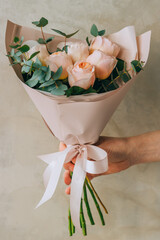 Bouquet of delicate peony roses of peach color with eucalyptus in a paper package. Summer background.