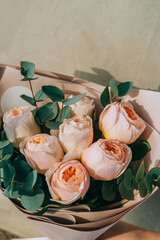 Bouquet of delicate peony roses of peach color with eucalyptus in a paper package. Summer background.