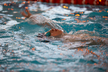 Boy in a swimming cap and swimming goggles in the pool. The child is engaged in the swimming section.