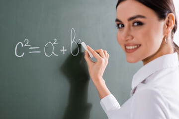 Blurred teacher smiling at camera while writing mathematic formula