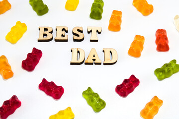 Text in wooden letters: best dad, with scattered colourful gummy bears isolated on white background, flat lay
