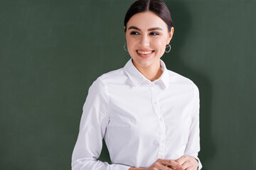 Young teacher in white shirt smiling near chalkboard