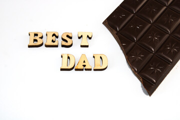 Text in wooden letters: best dad, with one piece of broken dark chocolate bar isolated on white background, card