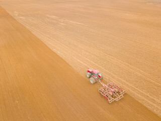 Fototapeta na wymiar Red tractor plows seeds or fertilizers in the field on a spring day. Photo with a drone