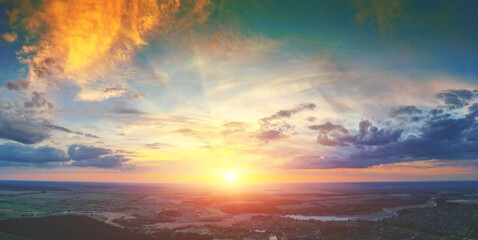 Beautiful sunset in the countryside in spring with the blazing sky. Rural landscape in the evening. Aerial view of brook, village, and arable fields. Panoramic view