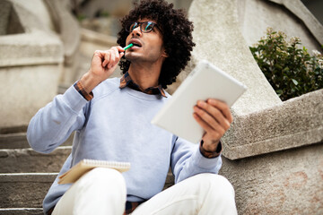 Obraz premium Young african businessman using tablet outdoors. Happy student learning outside.