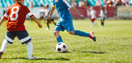 Obraz premium Children playing game on football soccer stadium field. Boys compete during soccer tournament match. Kids in red and blue soccer jersey shirts