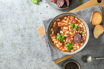 Asturiana traditional fabada with haricot, blood sausage served fresh crispy toast on gray stone table. View from above. Copy space. Spanish cuisine.
