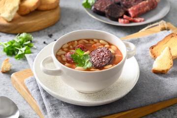 Spanish fabada with haricot, chorizo, morcillas, blood sausage served fresh crispy toast on gray stone table. Close up. Asturiana traditional cuisine.