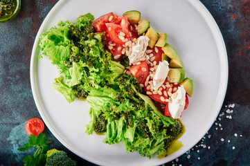Fresh salad with cherry tomatoes, feta cheese, avocado and pine nuts on white plate on blue oxidized background. Photo dishes for the menu. Top View