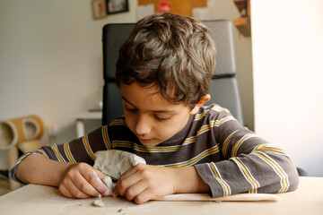 child playing with clay at home during quarantine. focused boy creating shapes with hands and using creativity and manual skills to mold toy shapes