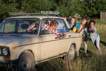 Young cheerful girls are pushing an old car. Women in the style of the 90s.