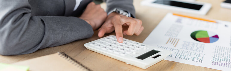 Cropped view of manager using calculator near paper with charts on blurred background, banner