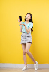 Young Asian girl holding smartphone on yellow background