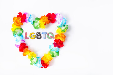 Hawaiian flower necklace in the shape of a heart with LGBTQ inscription inside on the white background. LGBTQ concept with rainbow flag colors. Pride month. Selective focus. Copy space.
