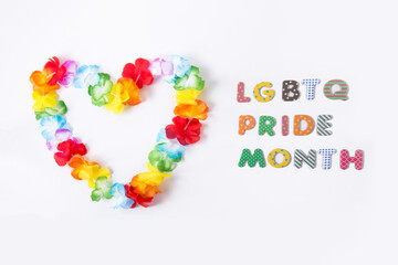 Hawaiian flower necklace in the shape of a heart with LGBTQ Pride month inscription on the white background. LGBT concept with rainbow flag colors. Selective focus. Copy space