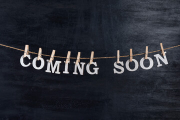 Obraz premium Words COMING SOON with clothespins on black background. Phrase from white letters.