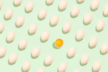 background of brown eggs with one broken in the middle on green background.