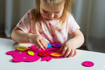 Little toddler girl buttoning a Montessori toy. Practical life skills, care of self, early education, activities and toy to develop the dexterity of child fingers, practical life, learning colors.  
