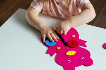 Little child hands buttoning a Montessori toy. Practical life skills, care of self, early education, activities and toy to develop the dexterity of child fingers, practical life, learning colors.