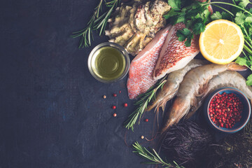 Seafood background: assortment with fillet of s sea bass, shrimp, langoustines, sea urchins, oysters with spices and herbs on a dark background. Rustic style, close-up
